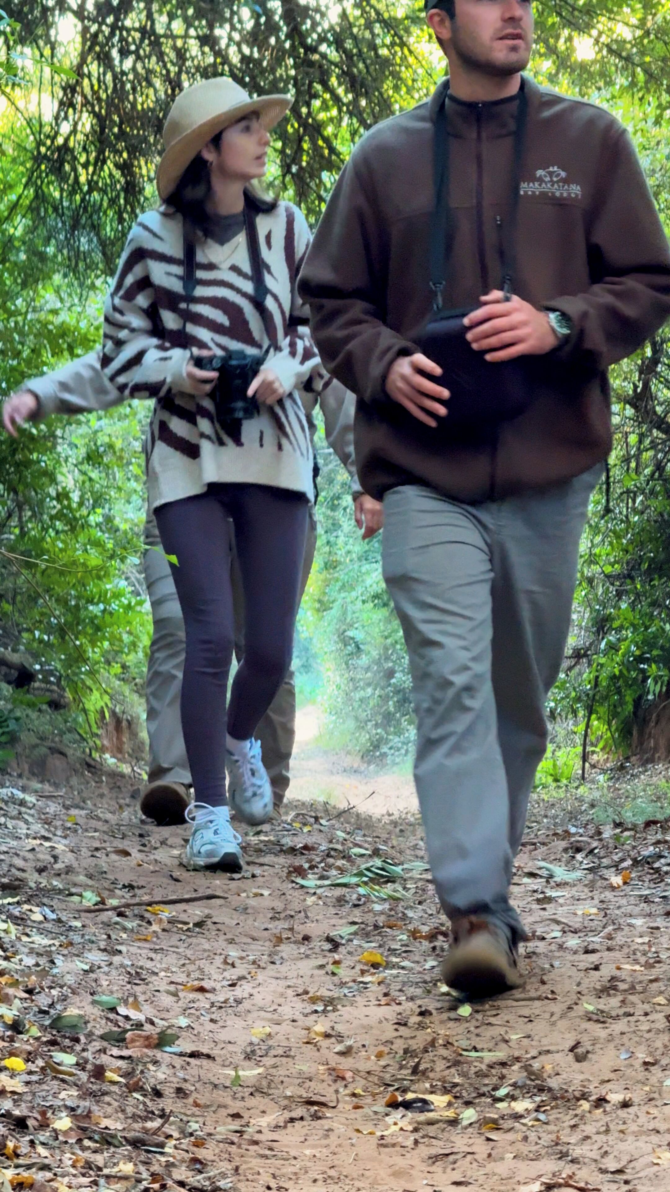 Two people walking on a dirt path surrounded by trees.