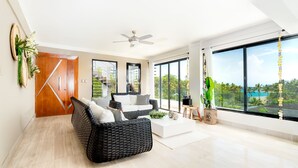A spacious living room with a large window, a ceiling fan, and a view of a tropical landscape. - 5 star BEACHVIEW PH W/ ROOFTOP TERRACE &JACUZZI (Las Terrenas)
