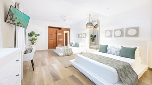 A modern bedroom with a large bed, a smaller sofa, a TV, and a wooden door. - 5 star BEACHVIEW PH W/ ROOFTOP TERRACE &JACUZZI (Las Terrenas)