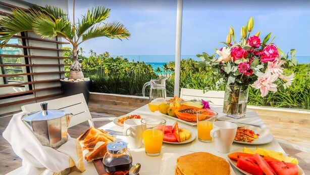 A breakfast table with toast, pancakes, fruit, and juice, set on a terrace with a view of the ocean. - 5 star BEACHVIEW PH W/ ROOFTOP TERRACE &JACUZZI (Las Terrenas)