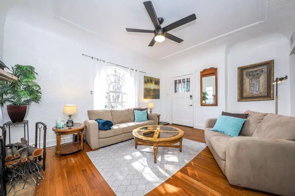 A living room with two sofas, a coffee table, a ceiling fan, a large window, and a door.