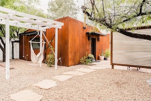 Una cabaña de madera con una hamaca, plantas en macetas y una estructura de metal corrugado.