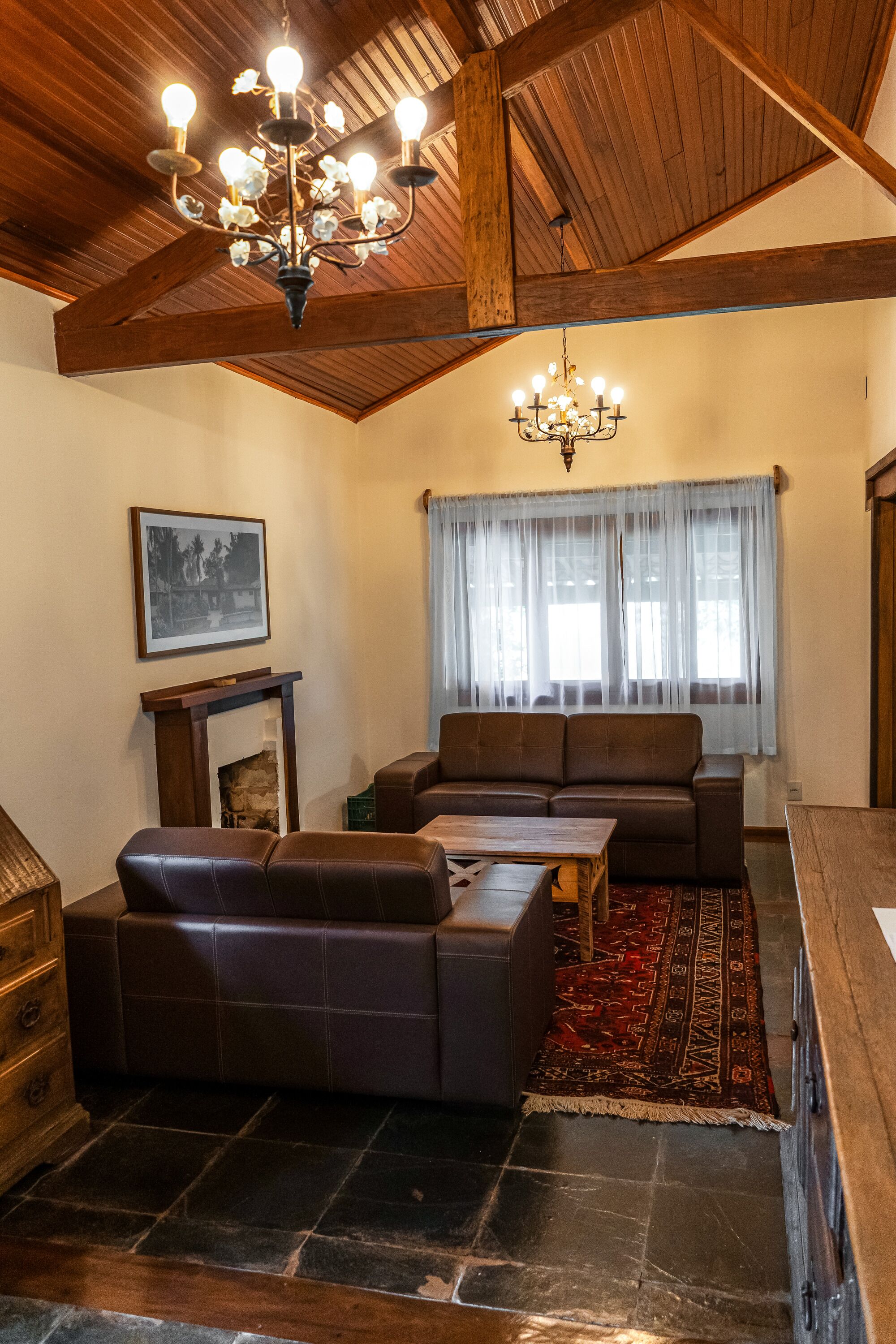 A living room with a brown leather sofa, a wooden coffee table, and a chandelier.