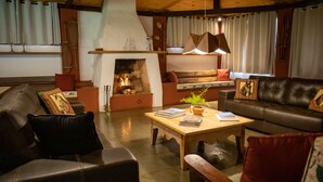 A cozy living room with a fireplace, leather sofas, a wooden coffee table, and a bookshelf. - Hotel Fazenda Bela Vista (Dourado)