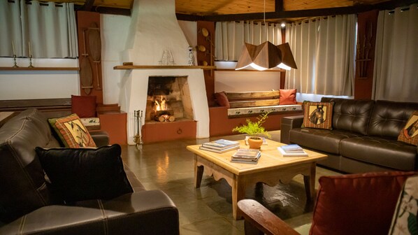 A cozy living room with a fireplace, leather sofas, a wooden coffee table, and a bookshelf. - Hotel Fazenda Bela Vista (Dourado)