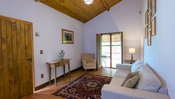 A cozy living room with a wooden ceiling, a white sofa, a patterned rug, a small table with a vase, and a chair.