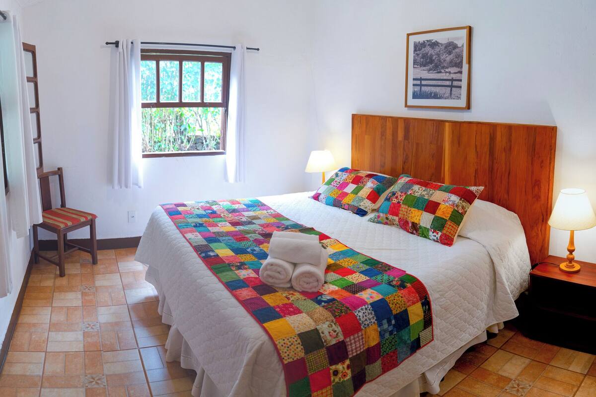 A neatly made bed with a colorful quilt, a wooden headboard, and a window with curtains.