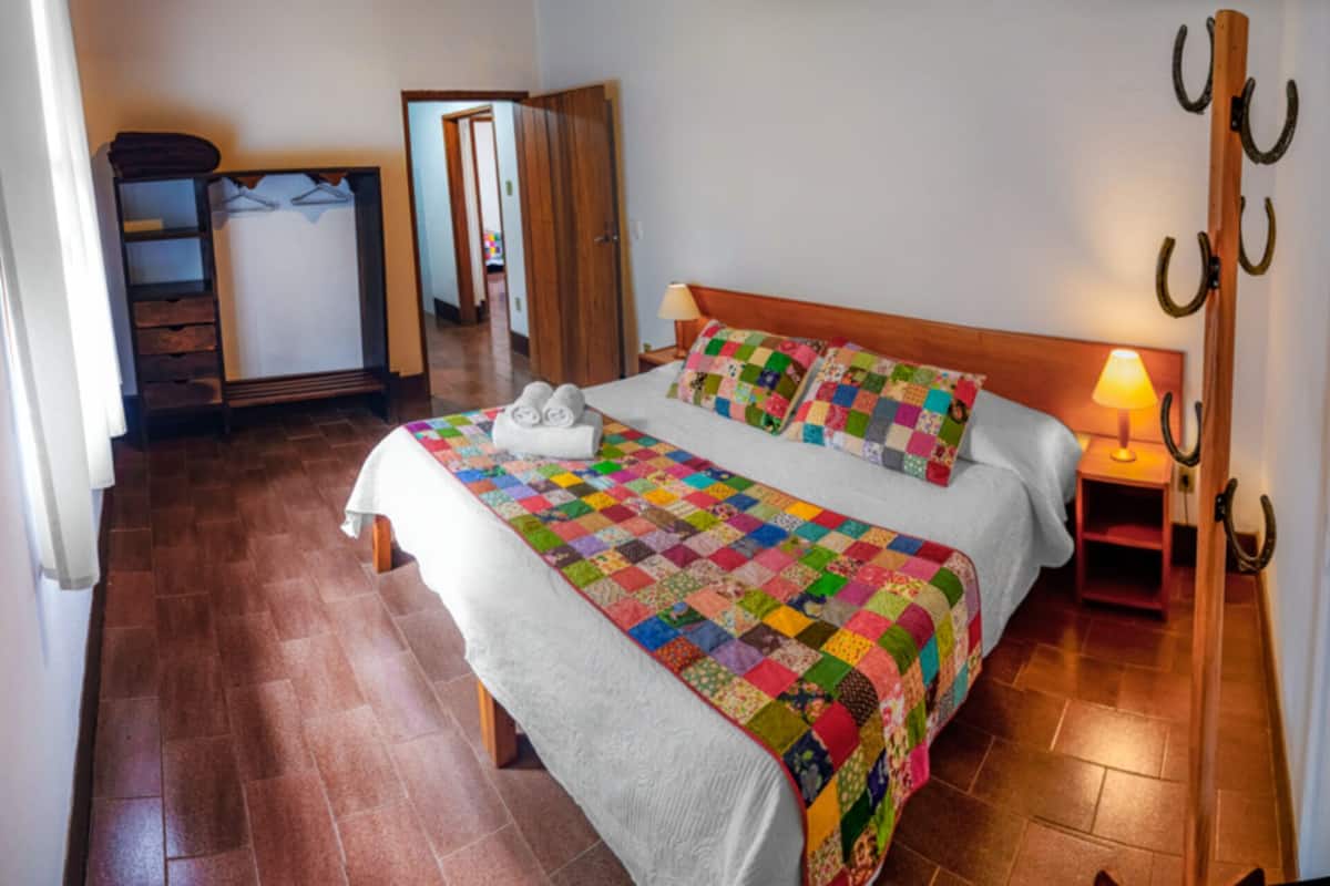 A neatly made bed with a colorful quilt, a wooden headboard, and a bedside lamp.