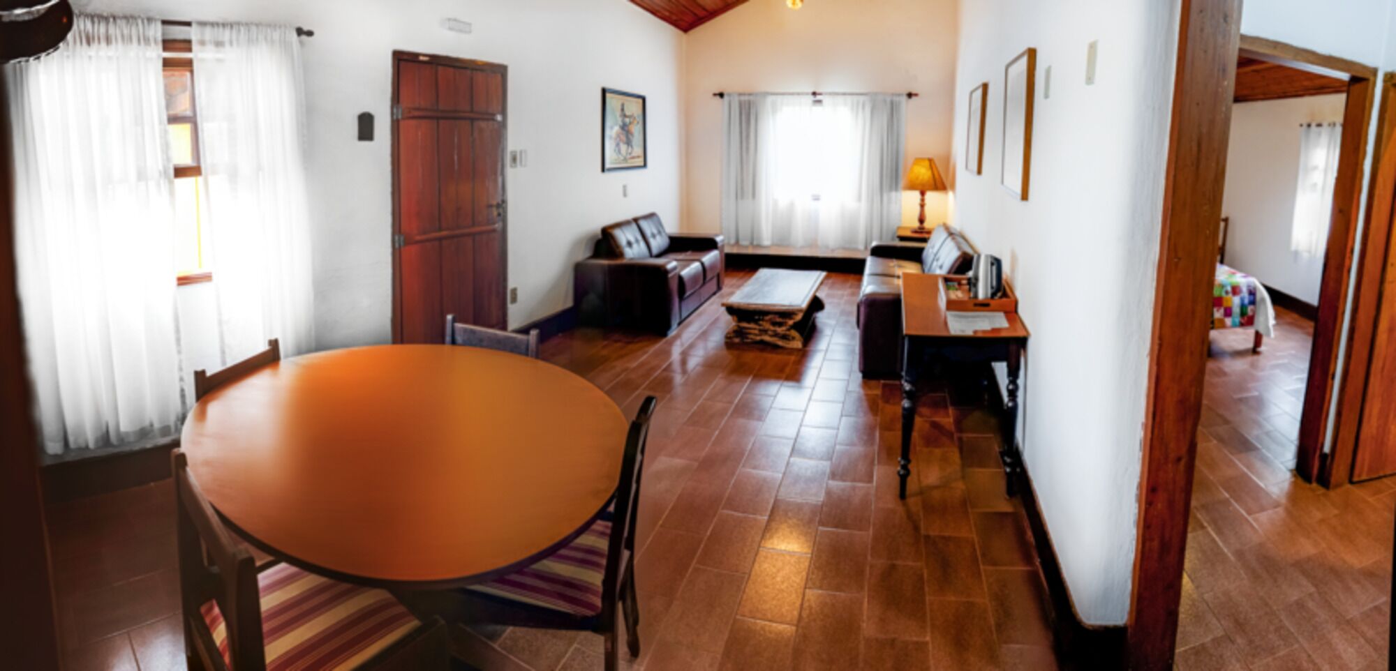 Amplia sala de estar con piso de madera, una mesa de comedor redonda, un sofá y una pequeña mesa de centro.