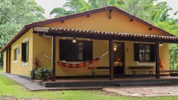 A yellow building with a tiled roof, a porch with a hammock, and a bench.