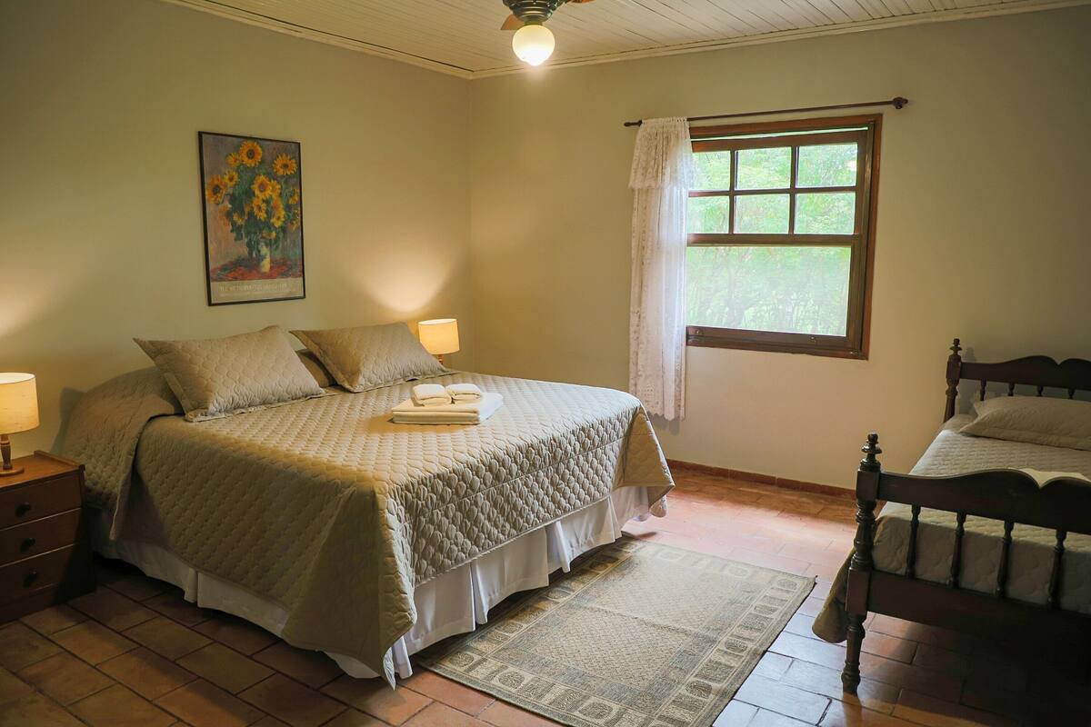 A bedroom with a bed, bedside lamps, a window with curtains, a painting on the wall, and a wooden floor.