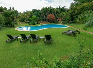 Una piscina rodeada de césped verde y árboles, con varias sillas de descanso dispuestas a su alrededor.