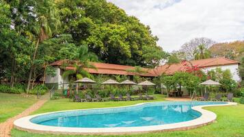 Una piscina con borde de azulejos, rodeada de césped y árboles.