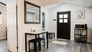 Un couloir avec une porte en bois sombre, un miroir, une petite table avec des chaises et une étagère sur laquelle sont posés divers objets.