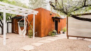 Un chalet rustique en bois, doté d’un hamac, d’une pergola et d’un chemin de gravier.