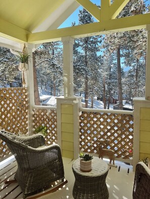 Relax in a serene outdoor space with a view of snow-covered trees, a wicker chair, and a small table.