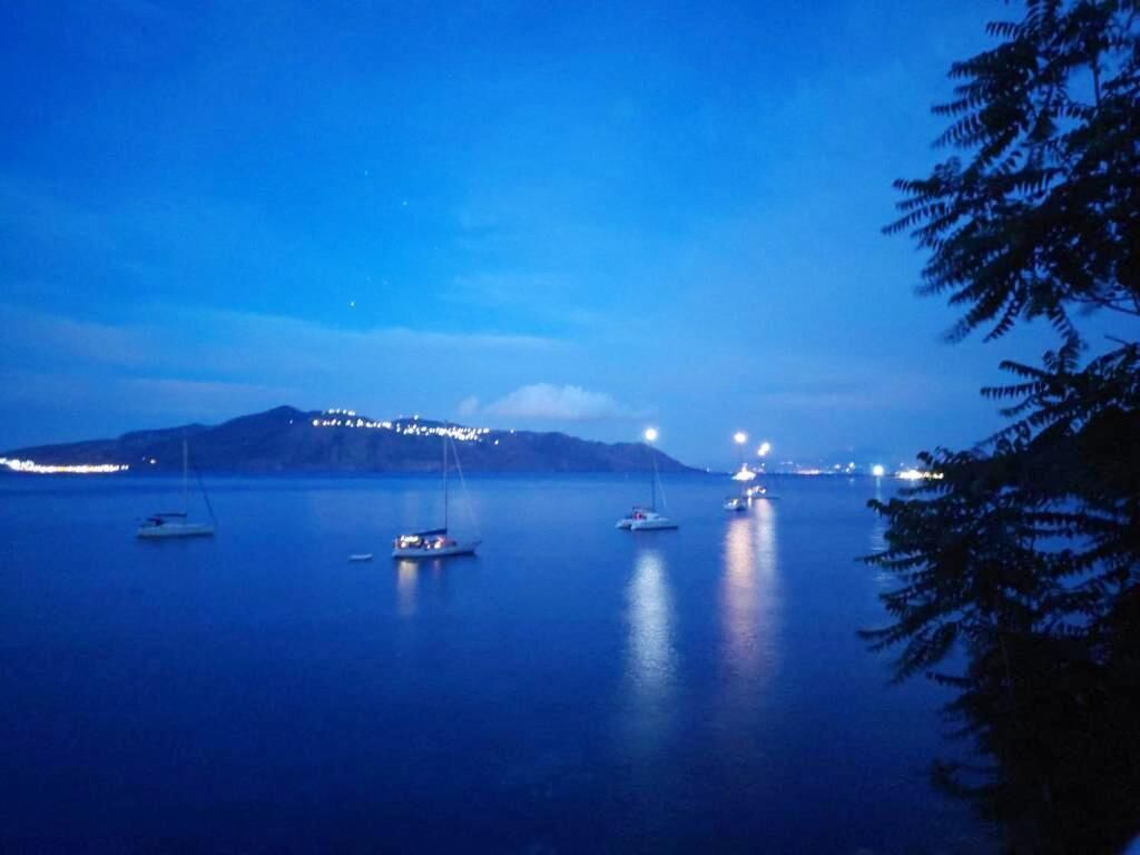 A calm body of water with several boats and distant city lights.
