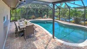 A covered outdoor area with a pool, a table set for dining, and wicker chairs. - Casa Das Palmas | Beautiful 3 Bed/2 Bath Home with screened Heated Pool | Minutes to Anna Maria Island Beaches | Sleeps 8 (Bradenton)