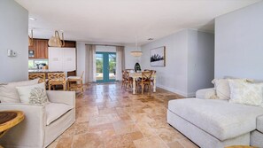 A spacious living area with a dining table and chairs, a kitchen with wooden cabinets, and a large window providing natural light.
