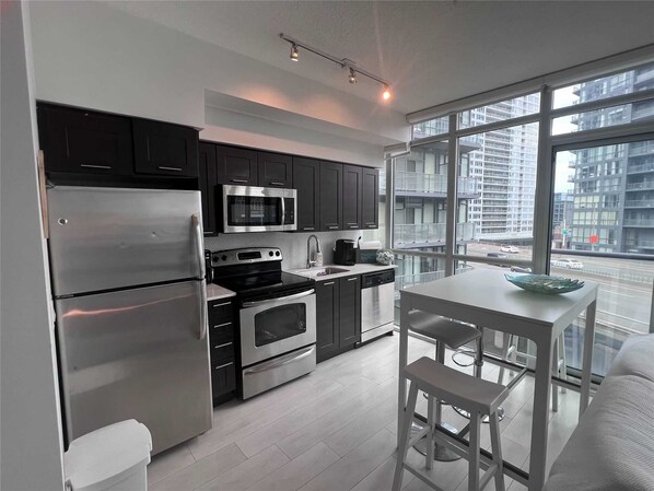Enjoy meals in the kitchen with stainless steel appliances and a dining area with a white table and bar stools.