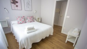 Un dormitorio ordenado con una cama grande, dos almohadas, una mesita de noche y un pequeño atril.