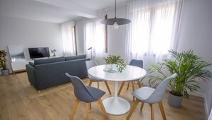 Una sala de estar moderna con un sofá gris, un televisor de pantalla plana y un comedor con una mesa redonda y sillas.