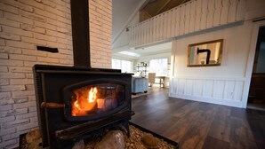 A modern living room with a wood-burning stove, a stone fireplace, and a large mirror on the wall. - The Lodge|Hot Tub|Horses|Hiking|Wood Stove (Groveland Township)
