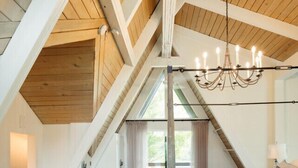 A bedroom with a sloped ceiling, a chandelier, a bed, and a view through a window. - The Lodge|Hot Tub|Horses|Hiking|Wood Stove (Groveland Township)