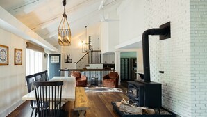 A spacious living room with a wooden dining table, black chairs, a fireplace, and a staircase leading to an upper level. - The Lodge|Hot Tub|Horses|Hiking|Wood Stove (Groveland Township)