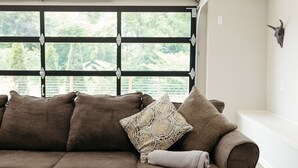 Una sala de estar moderna con un sofá modular, una mesita y un amplio ventanal con vistas a zonas verdes.