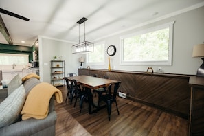 A modern kitchen with a dining area, wooden flooring, and large windows. - The Woods at Narrin Farms | Hot Tub | Horses | Kayaks | Hiking (Groveland Township)