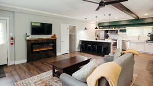 Una sala moderna con chimenea, un sofá y una mesa de centro. Se observa una zona de cocina con barra y una mesa de comedor.