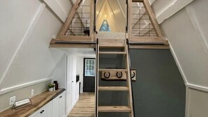 Camera mansarda con una scala in legno che conduce ad una zona notte soppalco, pareti bianche e pavimento in legno.