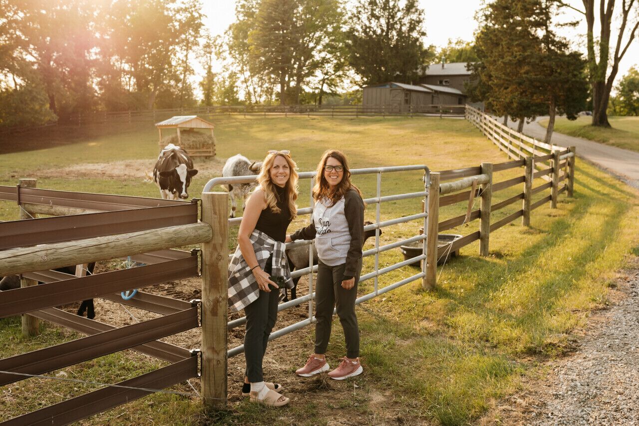 A wooden fence with a metal gate, a gravel path, and a barn in the background.
