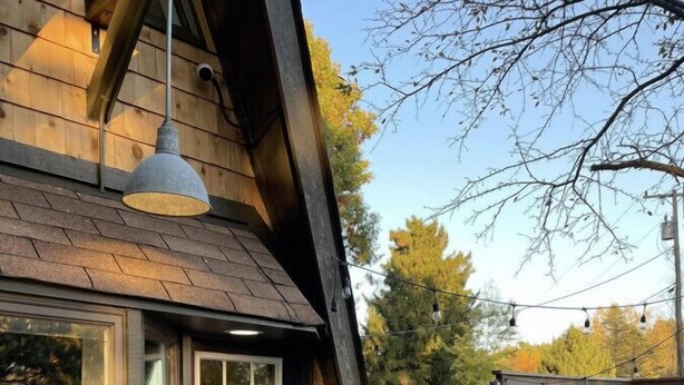 Una baita di legno con una porta d'ingresso scura, un piccolo portico e uno spazio esterno visibile, delimitato da una recinzione in legno.
