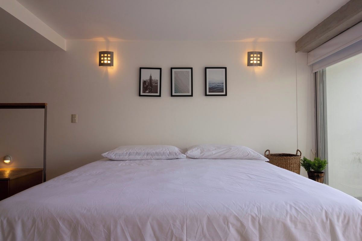 Une chambre à coucher avec un grand lit, une table de chevet, une lampe fixée au mur et une fenêtre donnant sur un beau paysage.