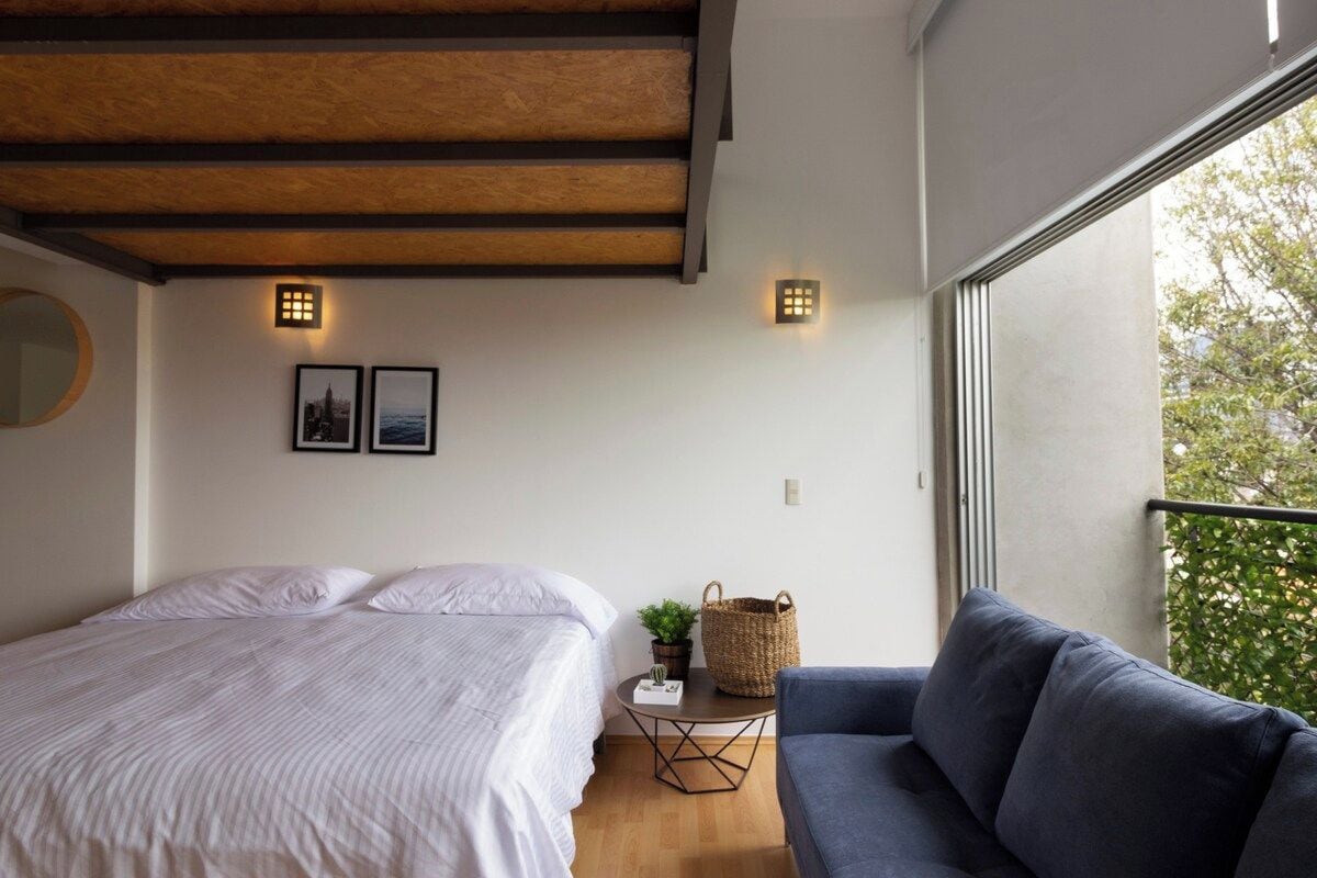 Een slaapkamer met een bed, een bank, een klein tafeltje met een plant en twee wandlampen.