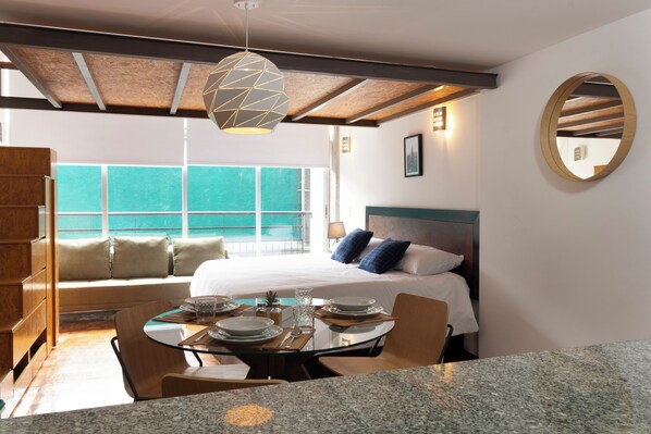 A hotel room with a bed, a dining table with chairs, a large window, and a ceiling light fixture.