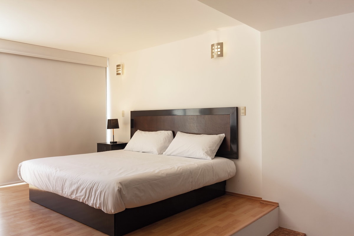 Een moderne slaapkamer met een groot bed, een nachtkastje en een wandlamp.