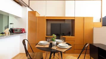 Cocina compacta con una mesa de comedor para dos personas, equipada con microondas, tostadora y una pequeña planta en maceta.
