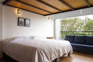 Een slaapkamer met een bed, een bank en een balkon met uitzicht op bomen.
