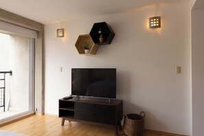 Een moderne woonkamer met een flatscreen televisie, houten vloeren, een schuifdeur met glas en twee zeshoekige wandlampen.
