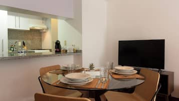 Uma área de refeições moderna com mesa de vidro, cadeiras de madeira e uma TV de tela plana.