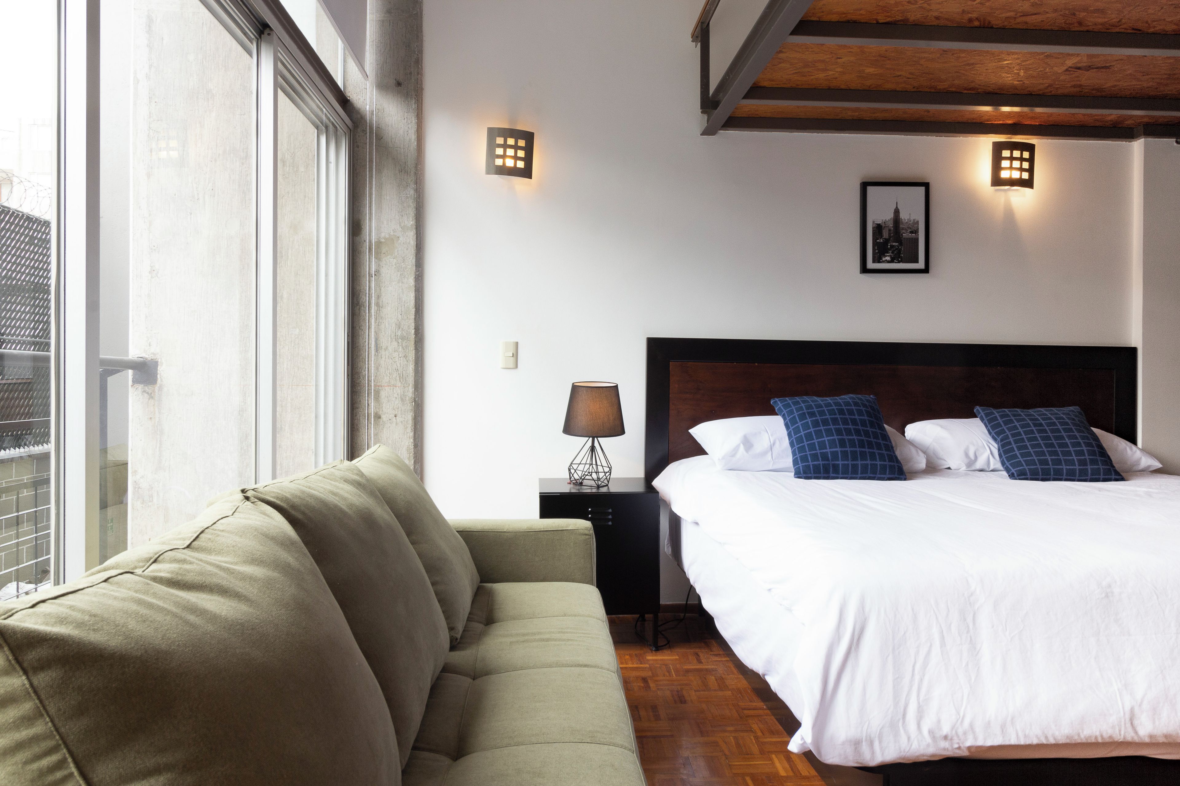 Quarto de hotel com cama, sofá, mesa de cabeceira e janela.