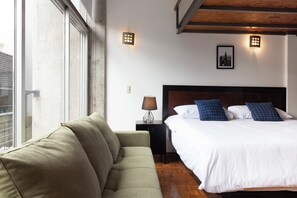 Una habitación de hotel con cama, sofá, mesita de noche y ventana.