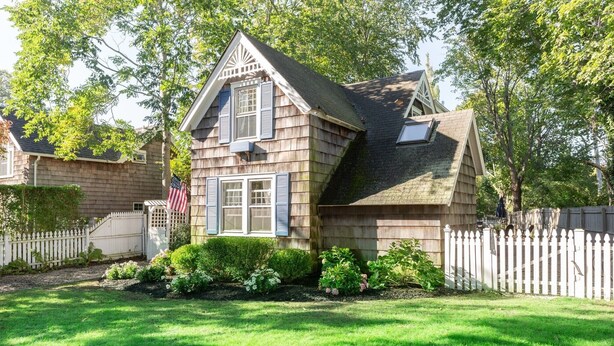 Een twee verdiepingen tellend huis met een puntige dakschild, een voortuin en een kleine tuin met verschillende planten en bloemen.