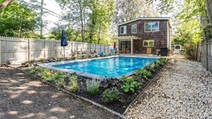 A house with a swimming pool, surrounded by a wooden fence and vegetation.
