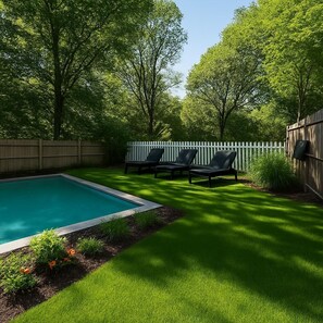 Patio con piscina, césped verde y valla de madera.