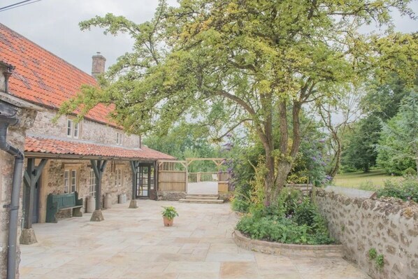 Sit and relax in the serene courtyard, surrounded by lush greenery and a large tree, with a covered seating area and potted plant.