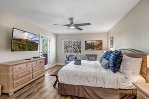 Une chambre avec un lit, une commode, un ventilateur de plafond et un téléviseur fixé au mur.